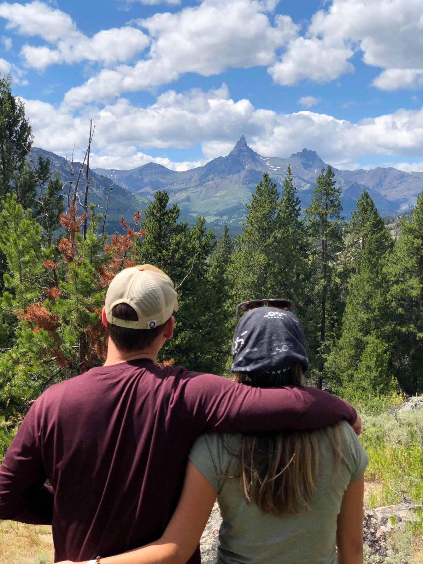 A couple with arms around each other looking out at a dramatic mountain peak