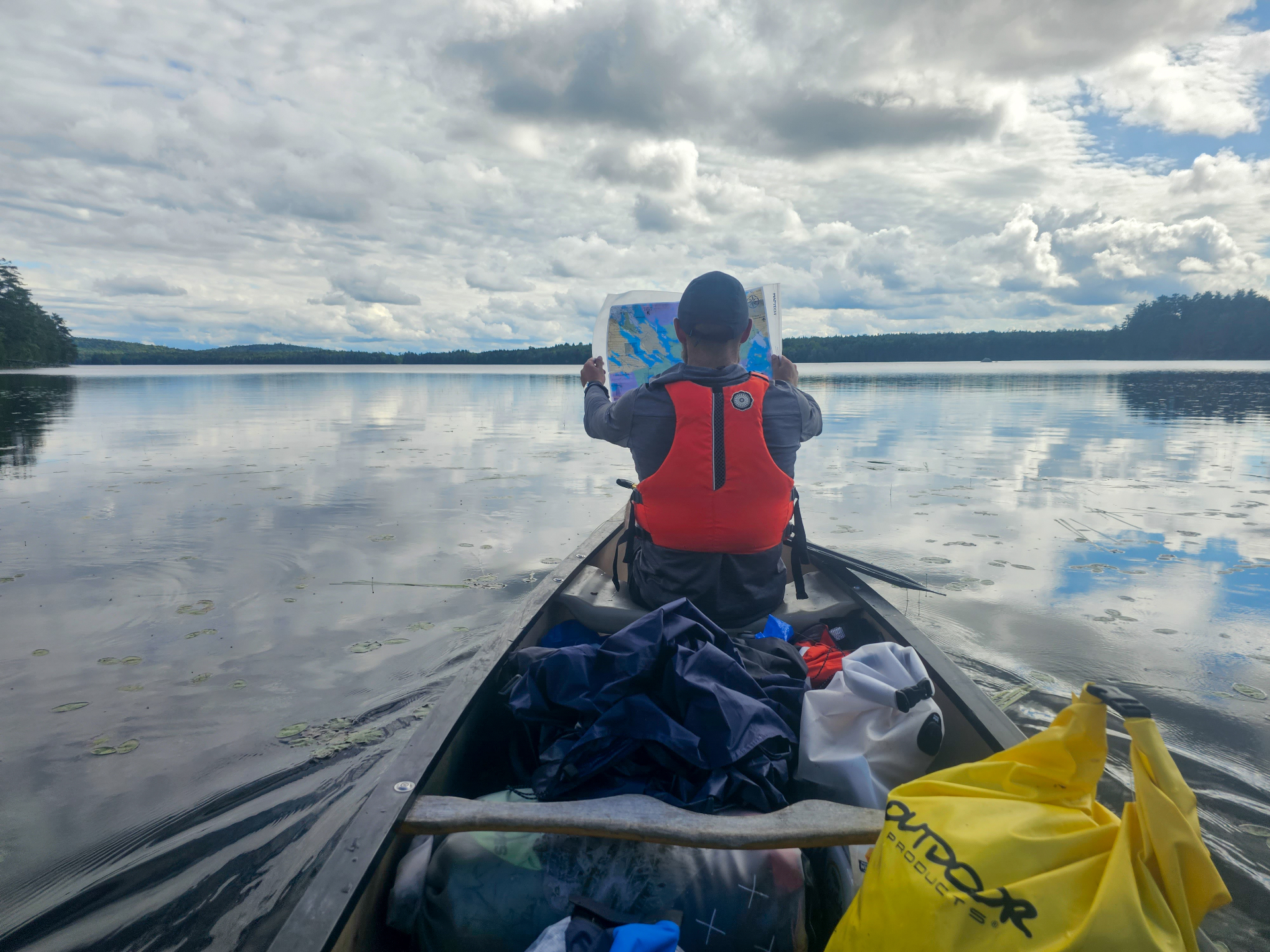 A paddler reading a map from the bow of a loaded canoe on a glassy lake