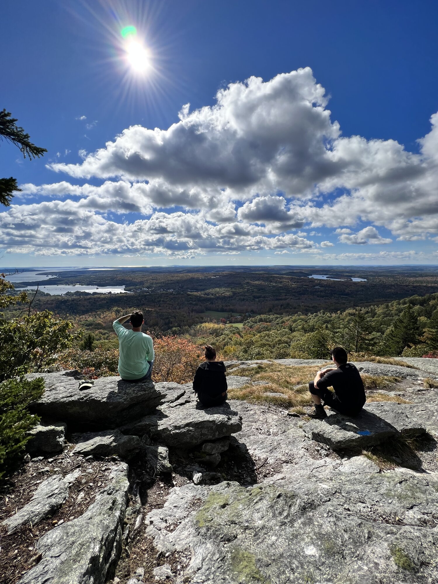 Three friends resting on a rocky summit with a sweeping view of lakes and forest
