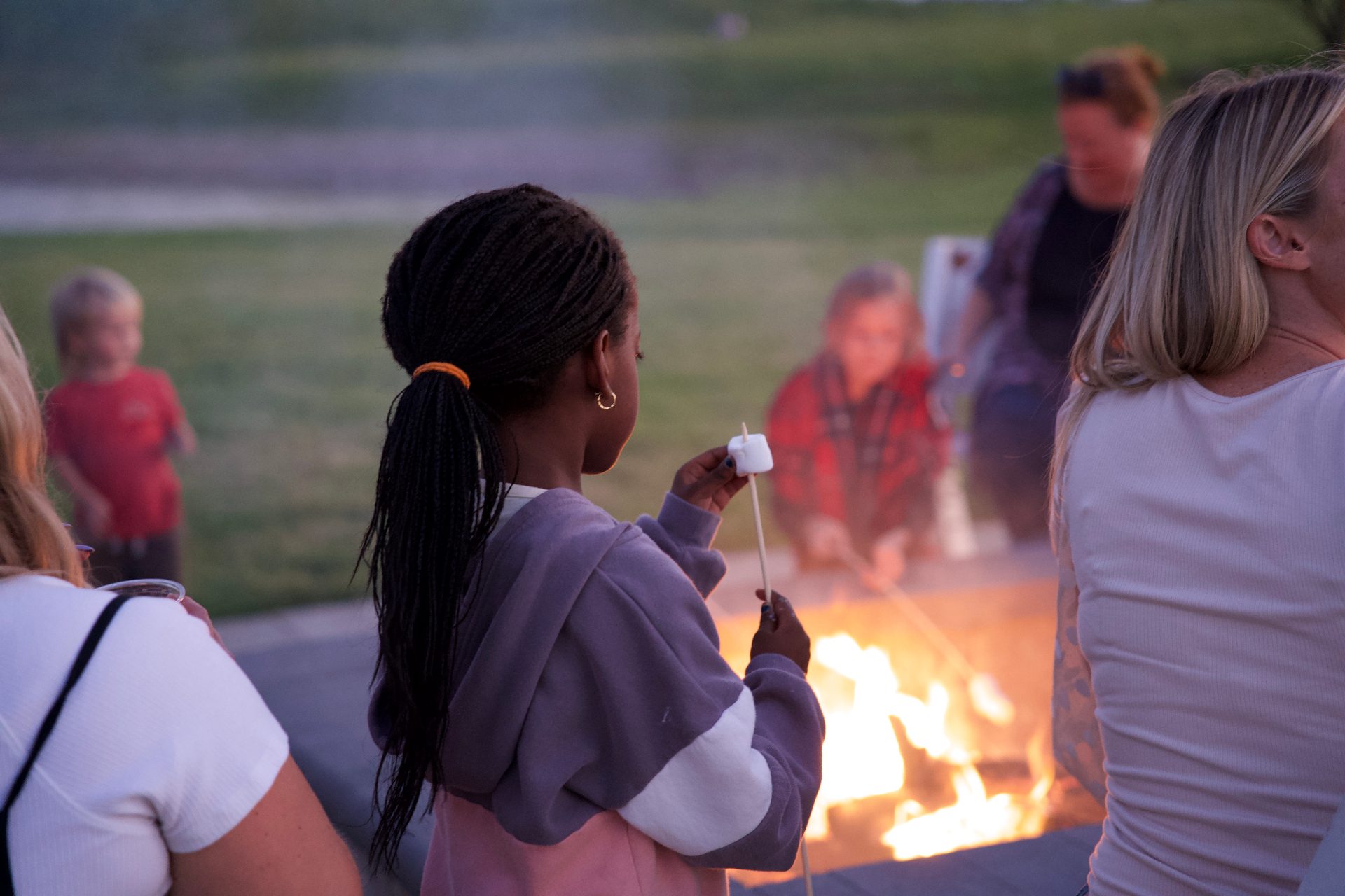 Family roasting marshmallows around a campfire at dusk