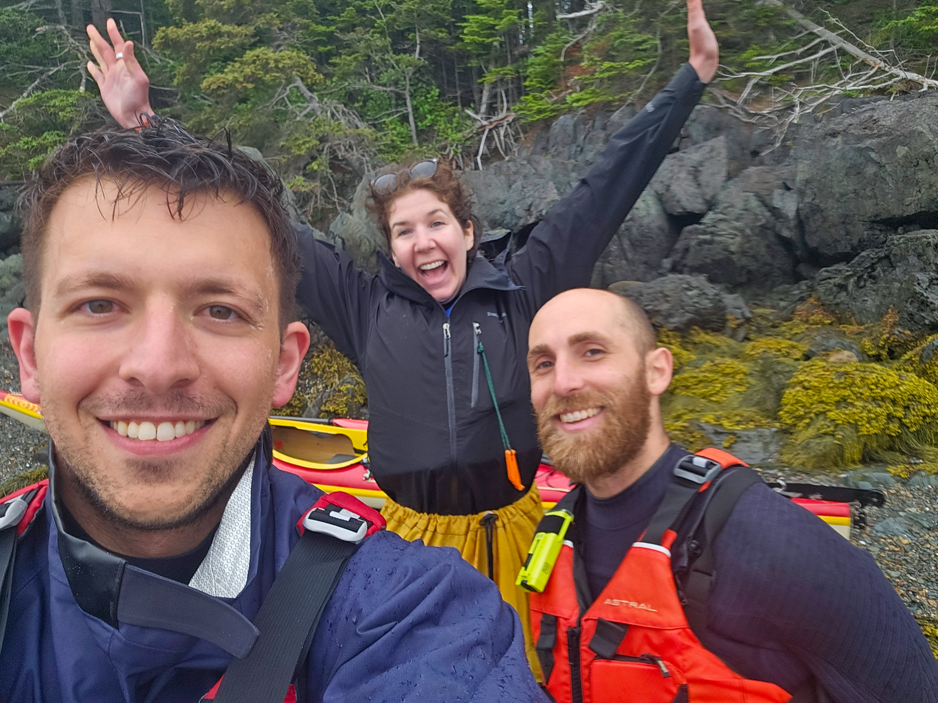 Three kayakers smiling on a rocky coastline after a paddle