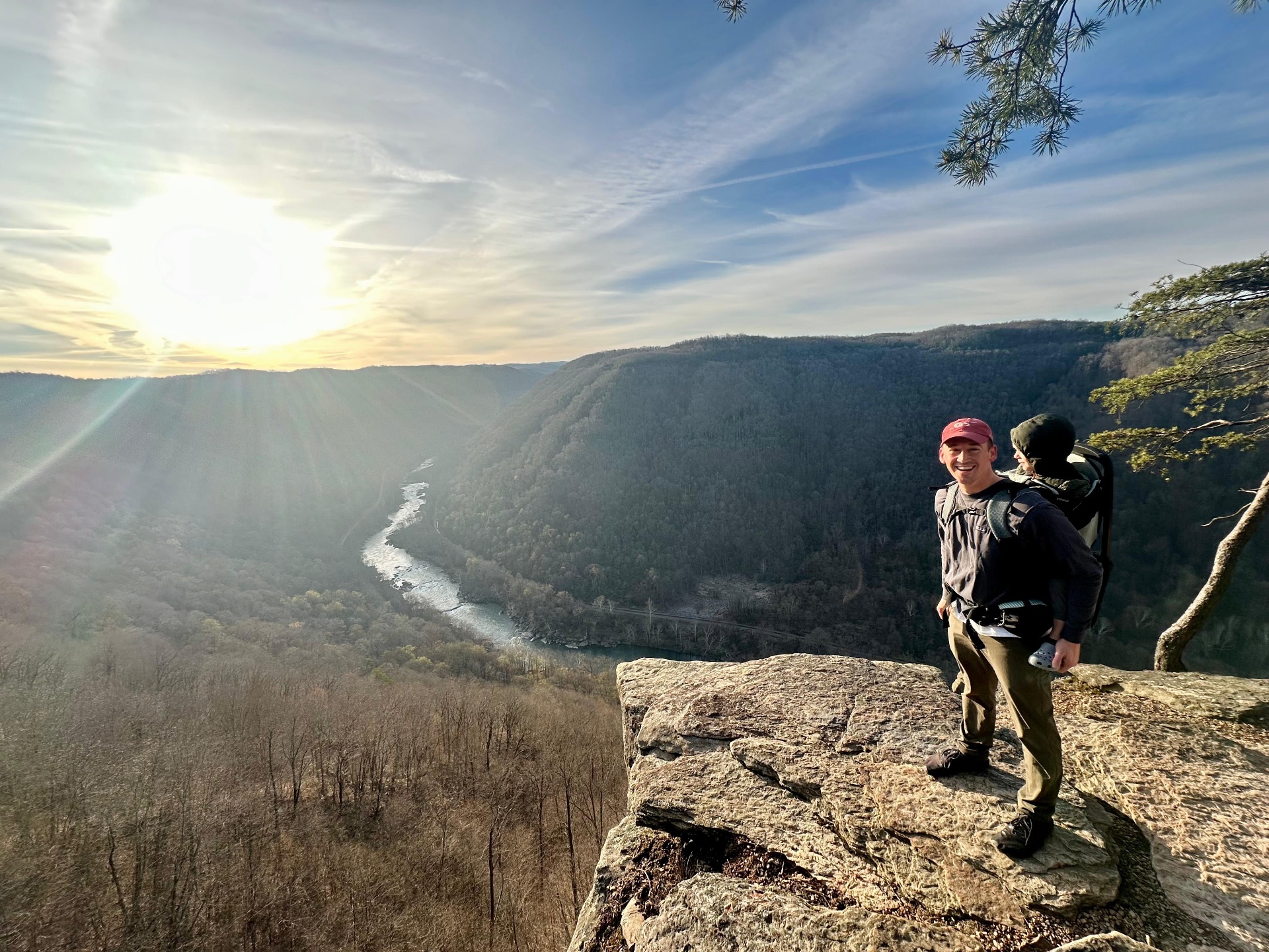 Hiker smiling on a clifftop overlook above a winding river at sunset