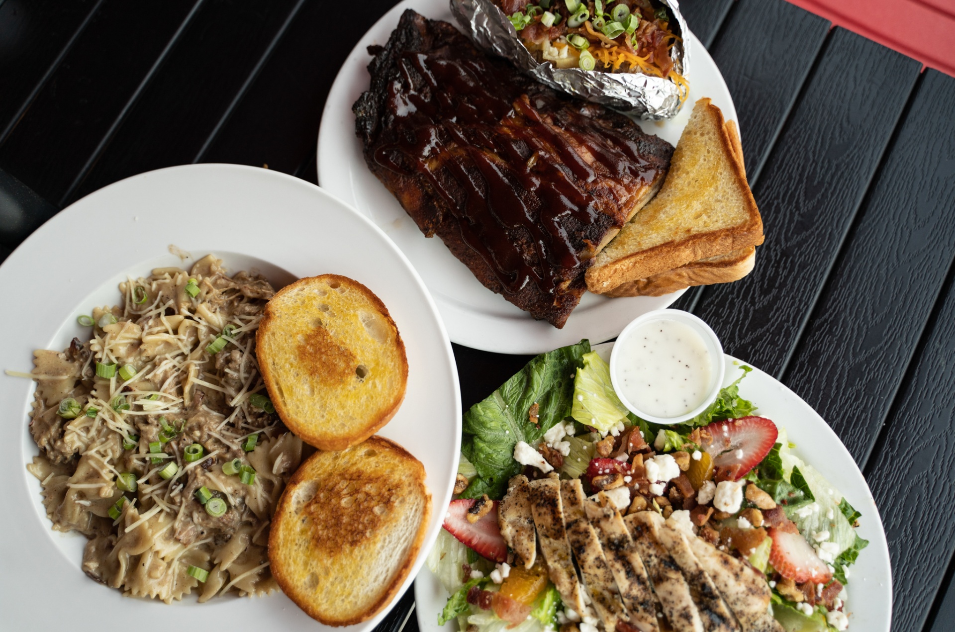An overhead spread of barbecue ribs, pasta, and a fresh salad at a local restaurant